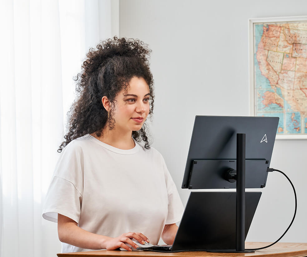 A woman is working from home with a desktop set up of a notebook and ZenScreen MB17AHG install on a tripod stand for a better comfortable viewing angle.