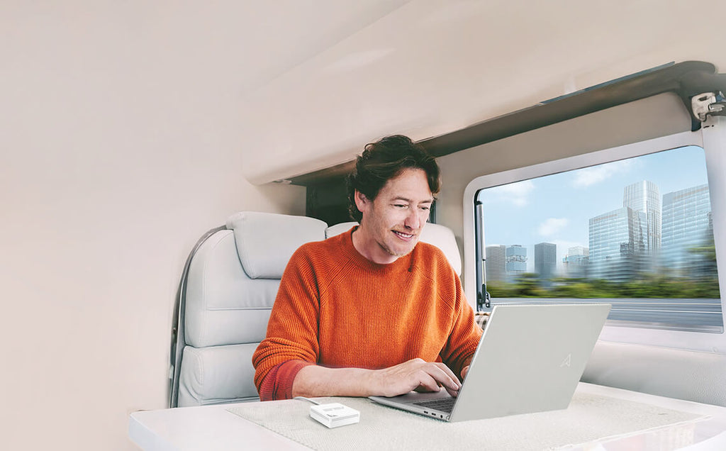 A man using laptop on a moving train, with a RT-AX50 Go on the table and the changing scenery visible through the window.