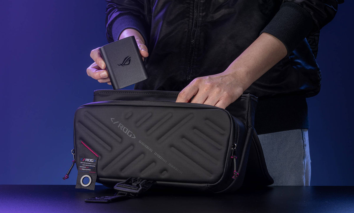 A person in a black jacket slipping the ROG 100W Gaming Charger Dock into an ROG Slash Sling Bag 4.0.